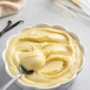 Crema pasticcera with a spoon in a serving bowl and a hand whisk in the background.