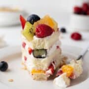 A single slice of fresh fruit cake with a fork on a white plate.