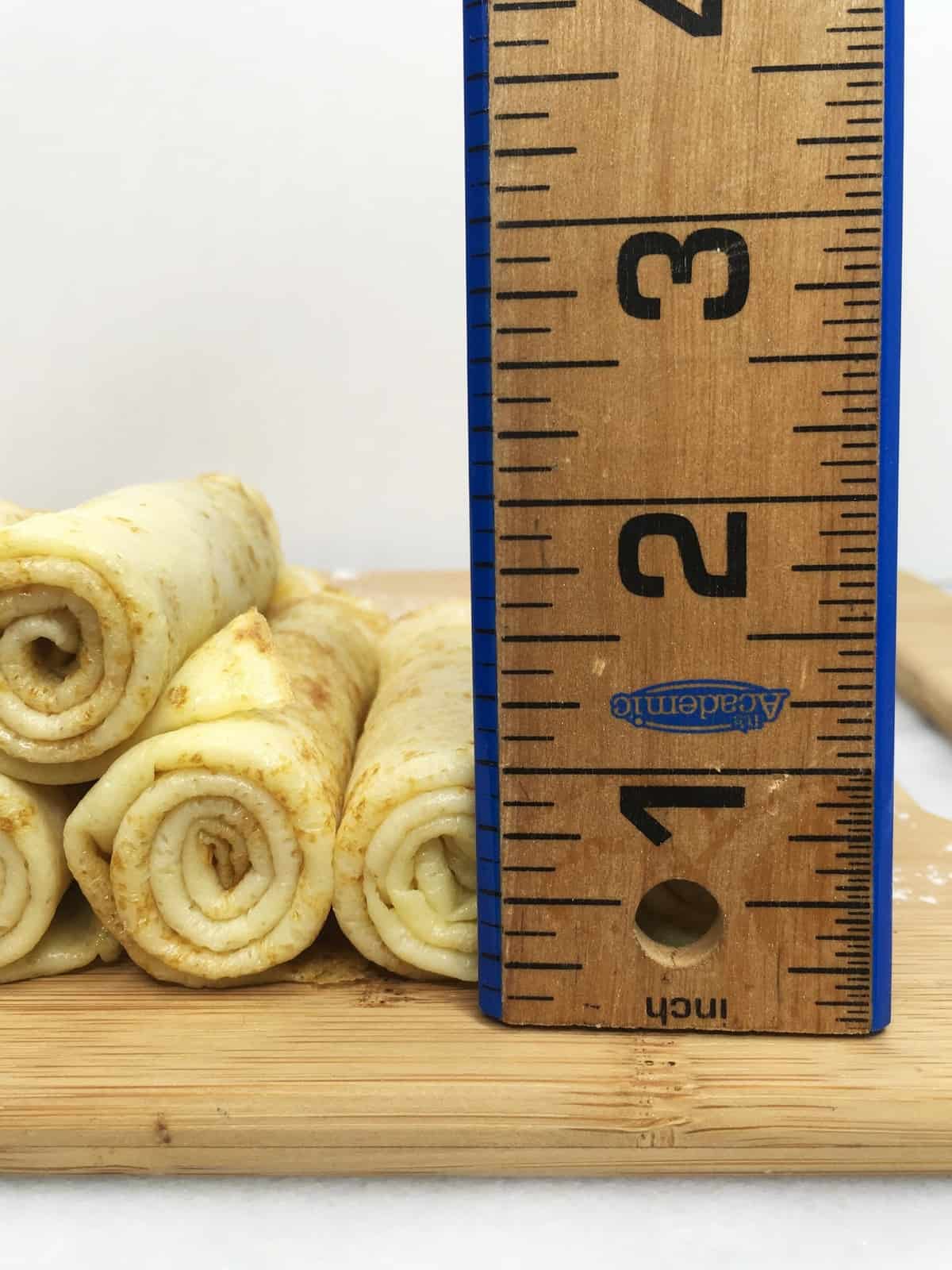 Rolled thin crepes with a wooden ruler on a board.