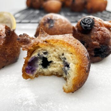 Bitten blueberry fritter with other fritters on a wire rack in the background