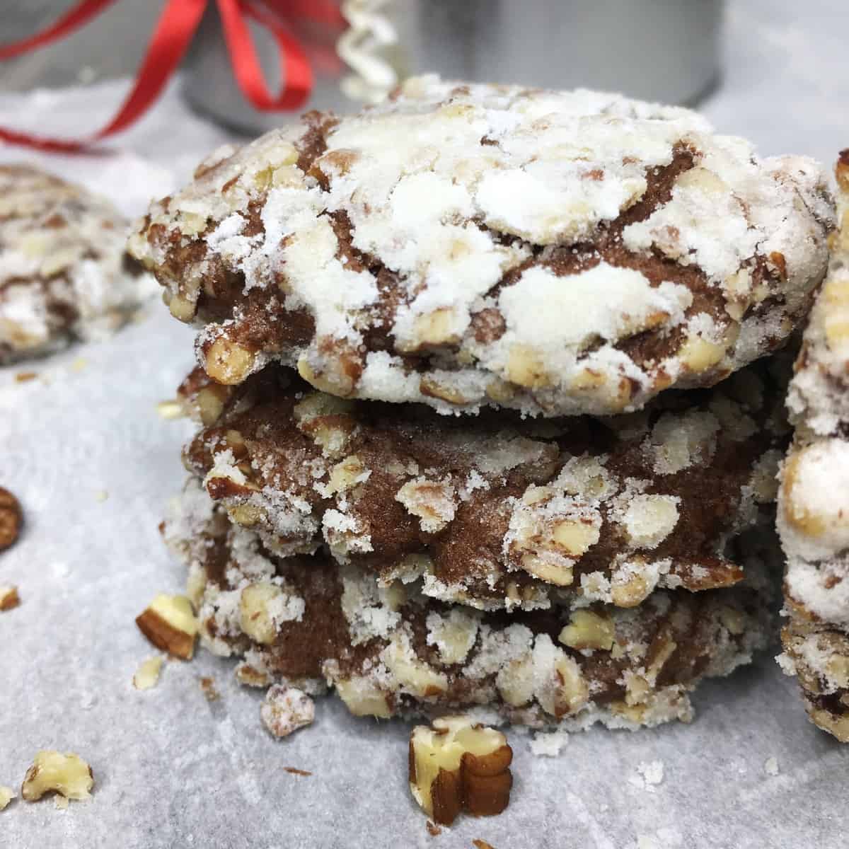 Stacked chocolate banana cookies with a gift tin and pecans in the background.