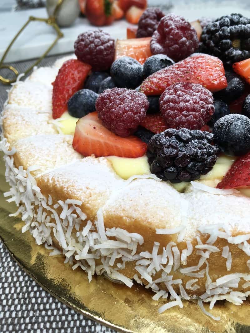 Coconut dacquoise cake topped with red fruit and sprinkled with icing sugar on a cake platter
