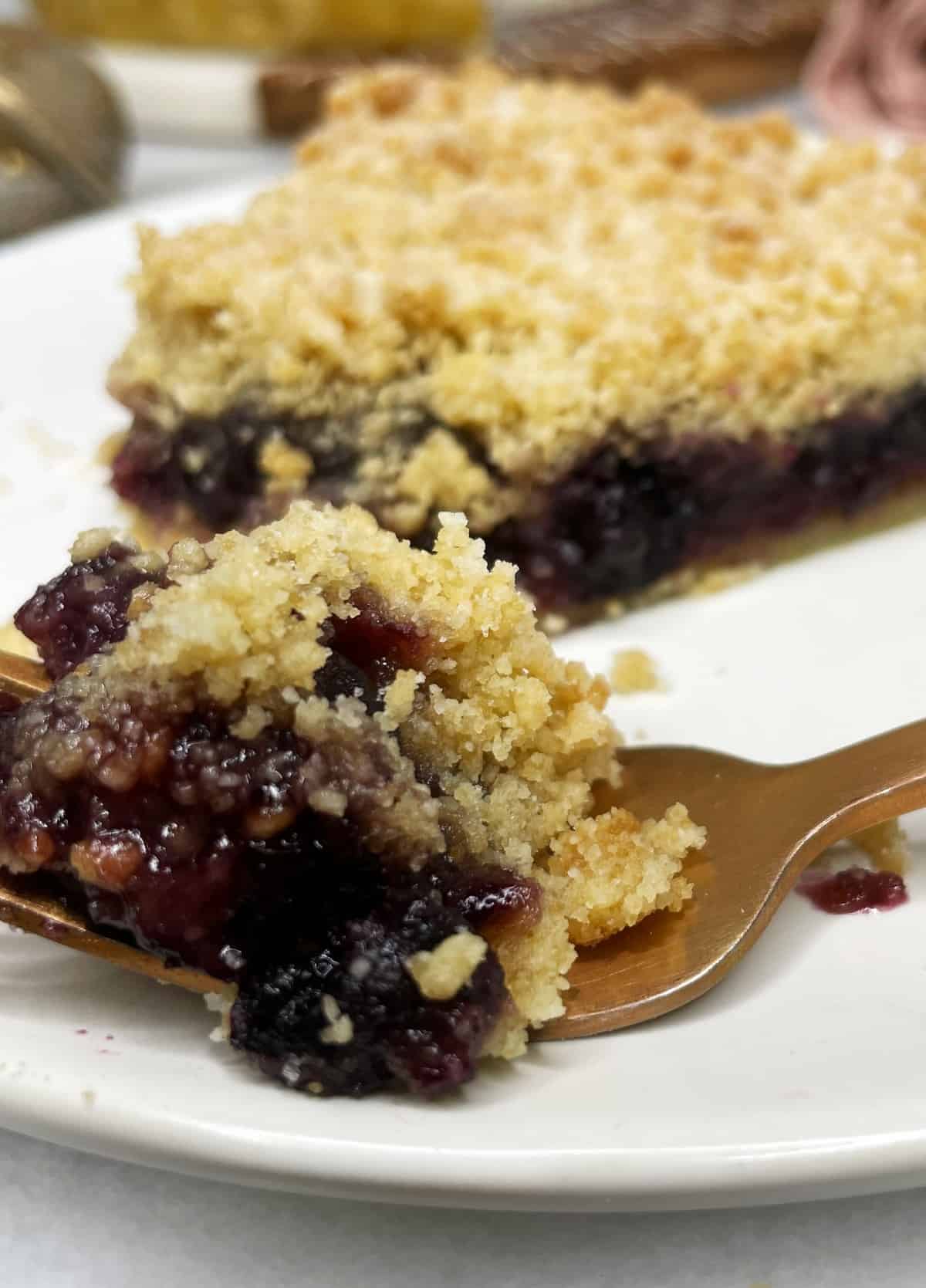 A fork with cherry pie and crumble with the rest of the slice on a plate