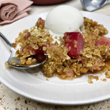 Baked rhubarb with oatmeal crisp and a scoop of ice cream on a white dessert plate