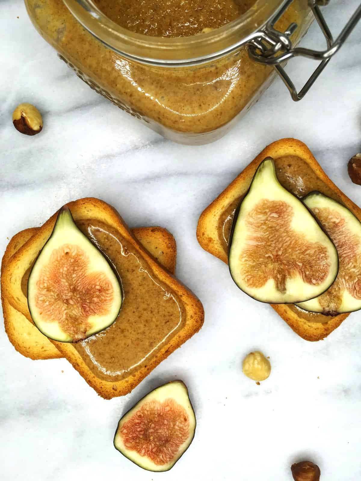 Two brioche toasts with praline paste, figs, and a glass jar on a marble board