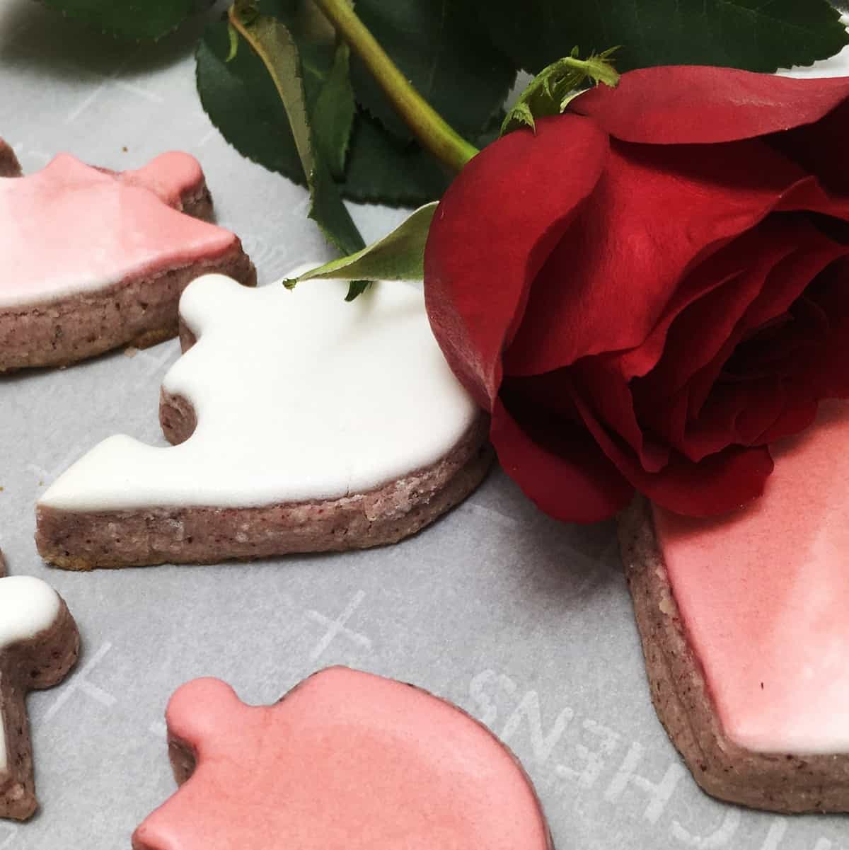 Whole heart-shaped and puzzled cookies with a rose on the parchment
