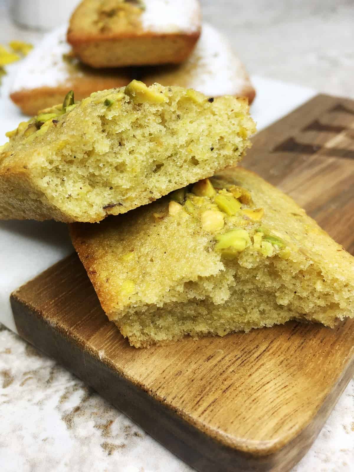 Sliced pistachio financier with three cakes and a cup on background