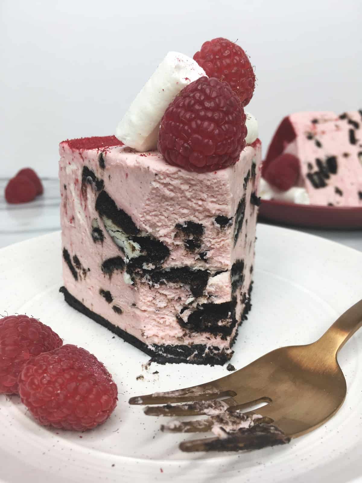 A single slice of no-bake Oreo cheesecake, fork, and raspberries on a white plate