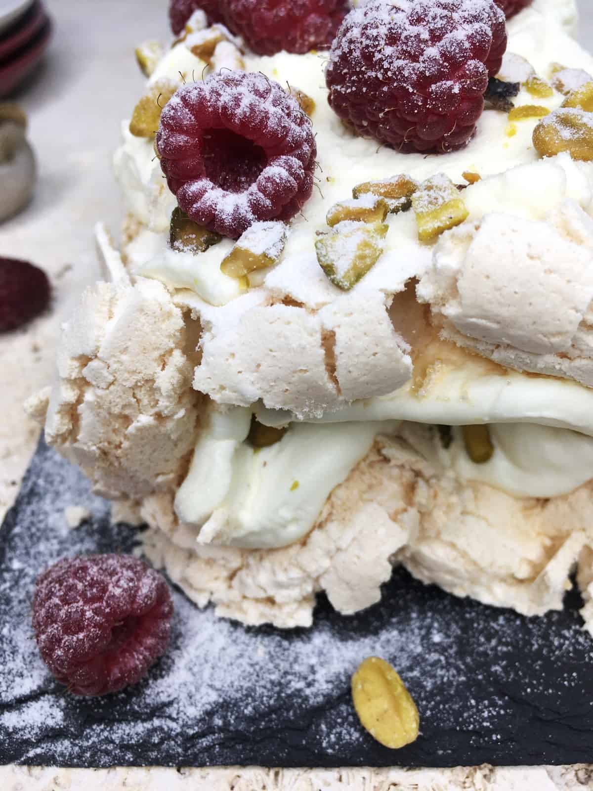 Decorated rosewater meringue roulade on a black serving board with plates in the background
