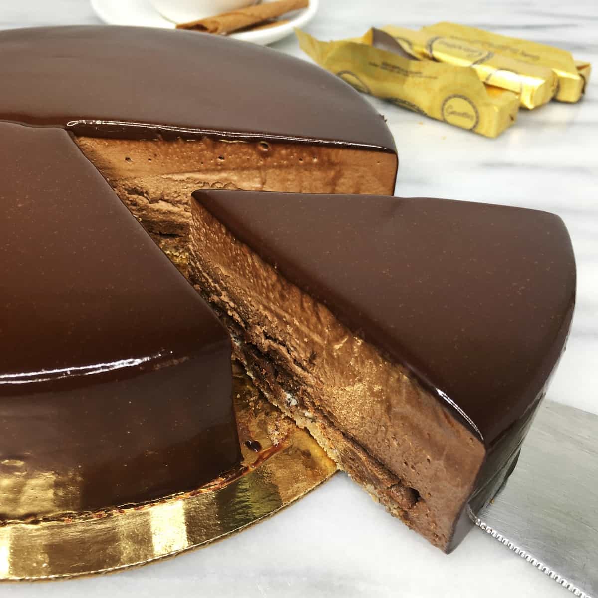 Sliced Royal chocolate cake on a golden cake board with crepes Gravottes on background