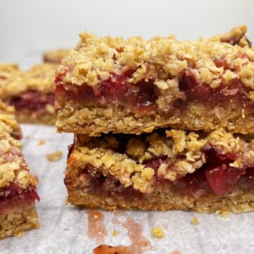 Two stacked strawberry bars made with crumble on parchment.