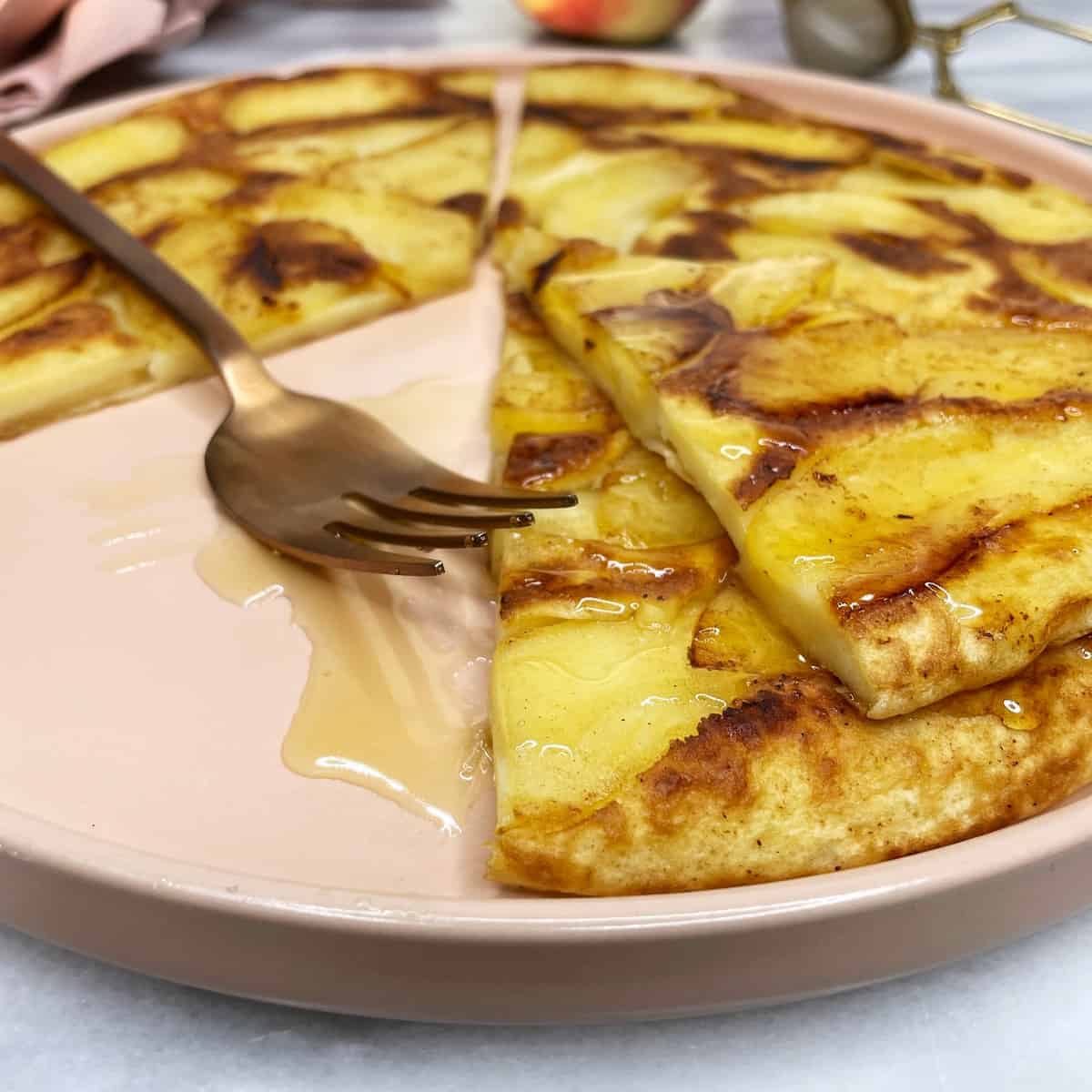 Sliced upside-down apple pancake topped with honey on a pink plate with a fork 