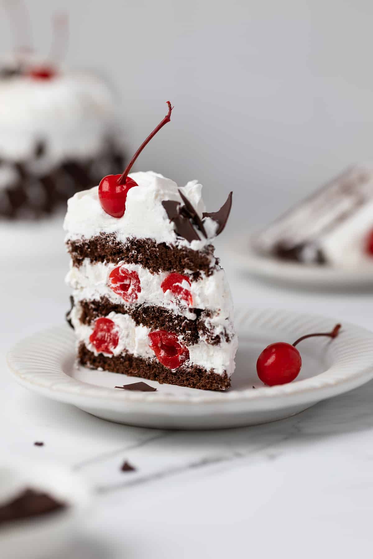 A single slice of Black Forest cake on a white dessert place. 