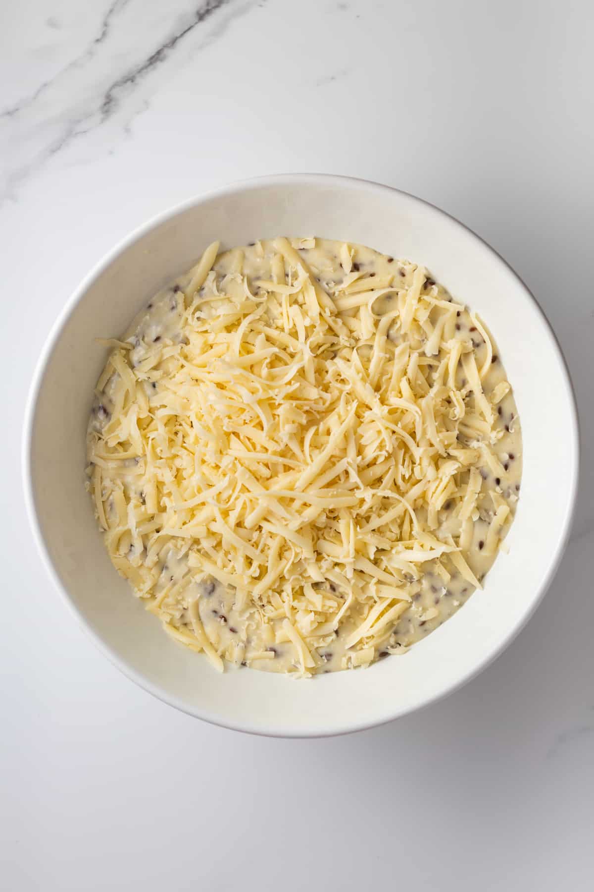 Cake batter topped with grated cheese in a mixing bowl.