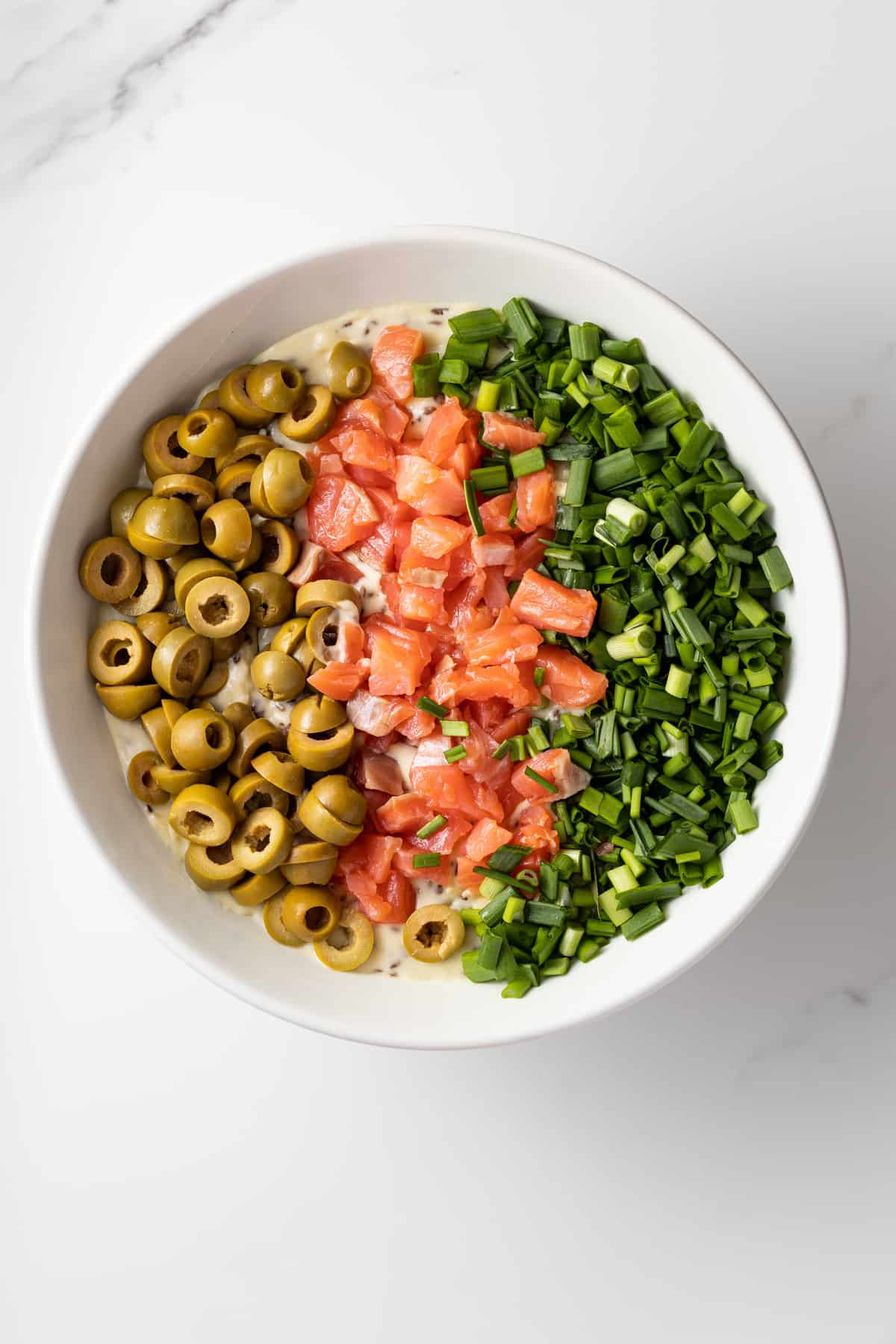 Cake batter topped with green onions, salmon and olives in a bowl.