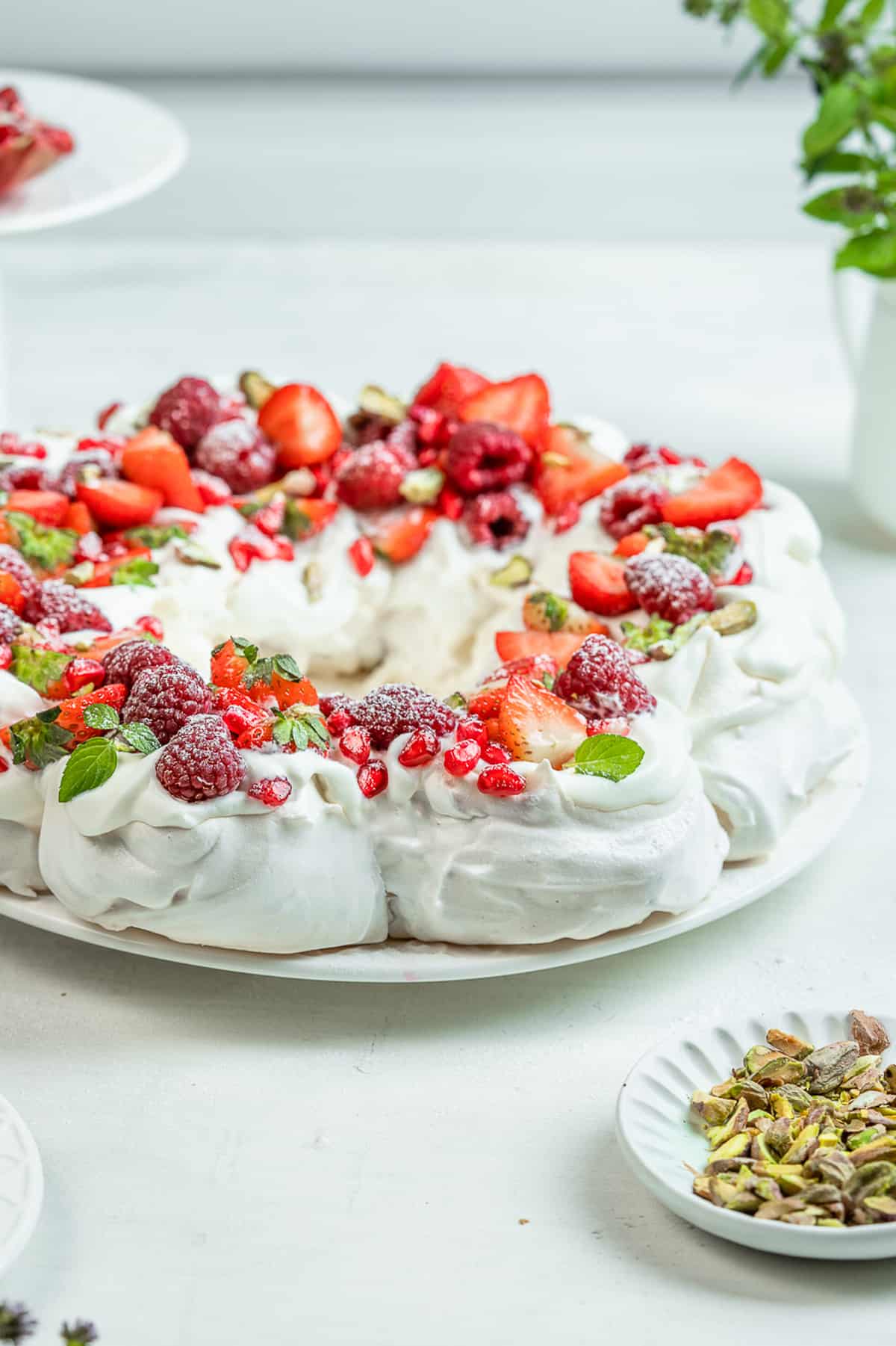 Meringue wreath with red fruit on top on a serving plate.