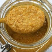 Glass jar with hazelnut spread over a spoon.