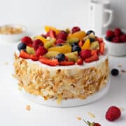 Fresh fruit cake on a serving plate with fresh berries in the background.