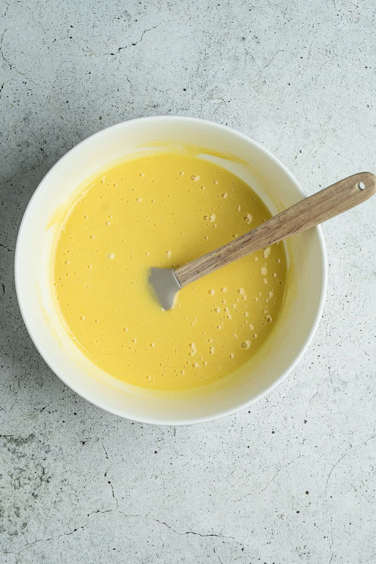 Egg yolk mixture with a spatula in a bowl.