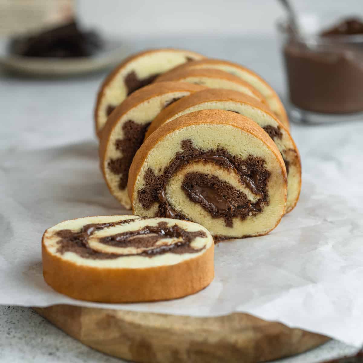Slices of Nutella Swiss roll on a wooden board lined with parchment.