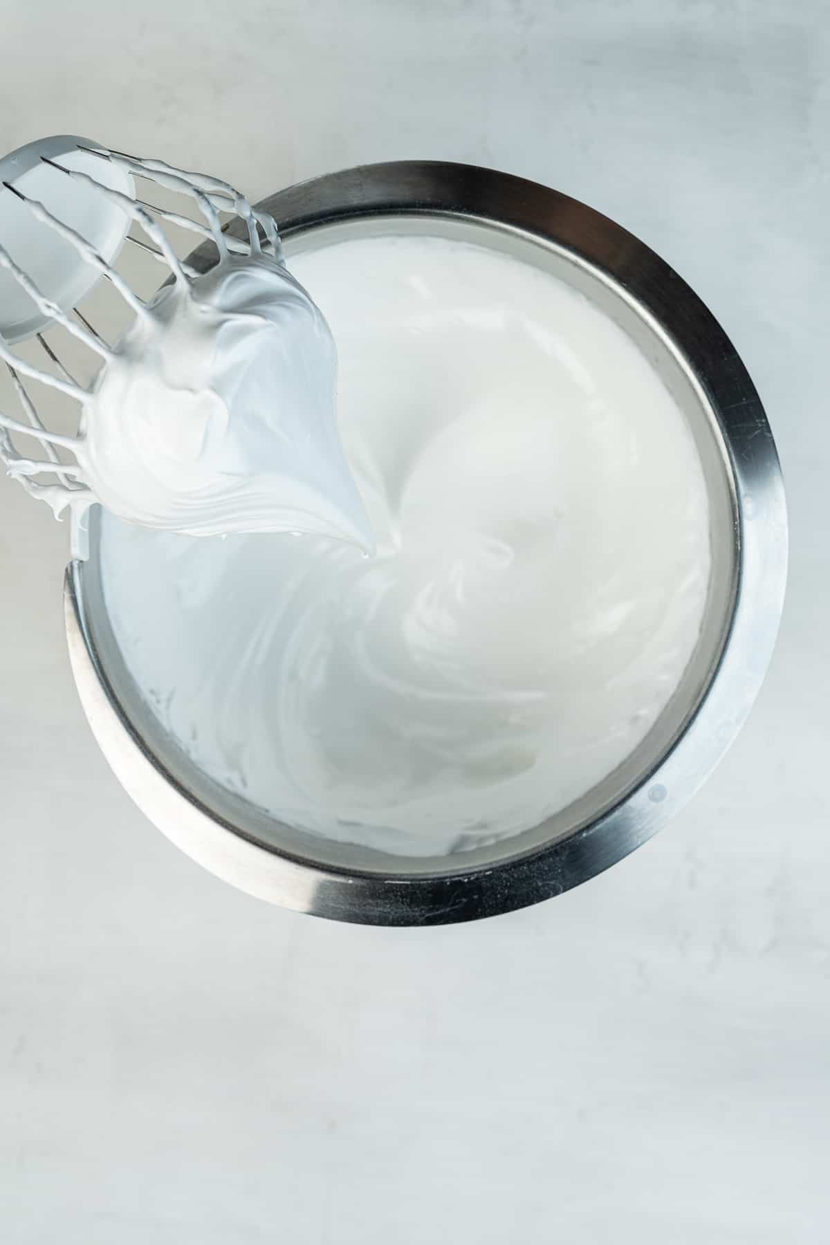 Meringue with a stiff peak on a mixer beater over the bowl.
