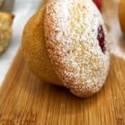 A financier cake with raspberry dusted with icing sugar on a wooden board.