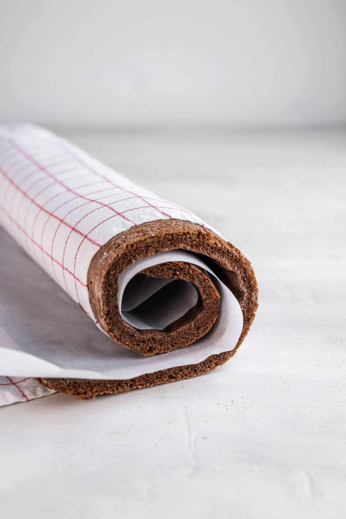 Chocolate sponge rolled in a kitchen towel and parchment paper.